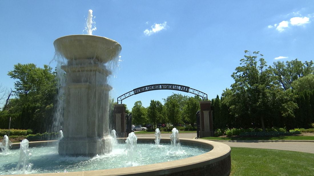 A fountain spurting water is at the foreground of the photo. In the background, there is a gated archway with the words "George George Memorial Park" on the archway